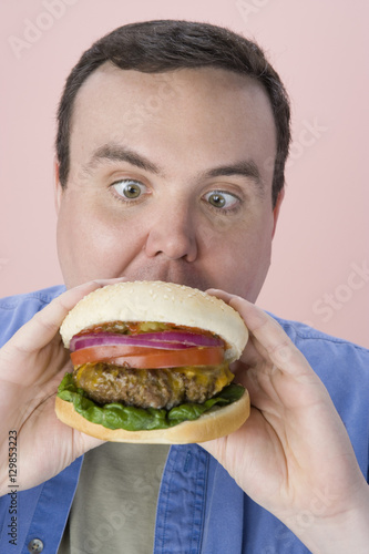 Middle aged man eating hamburger over pink background