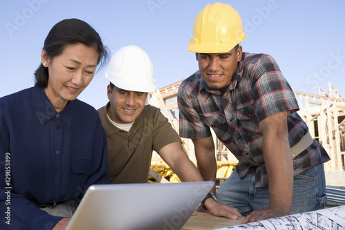 Female architect with workers using laptop at construction site