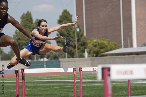 Multiracial female athletes clearing hurdles in race