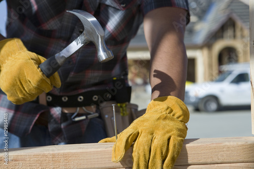 Fotografia, Obraz Closeup of man's hands hammering nail into wooden plank at site