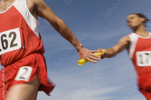 Male athletes passing baton in relay race photo