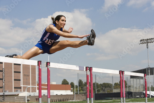 Determined female athlete jumping over a hurdles photo