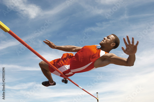 Low angle view of a male high jumper in midair over bar against the sky