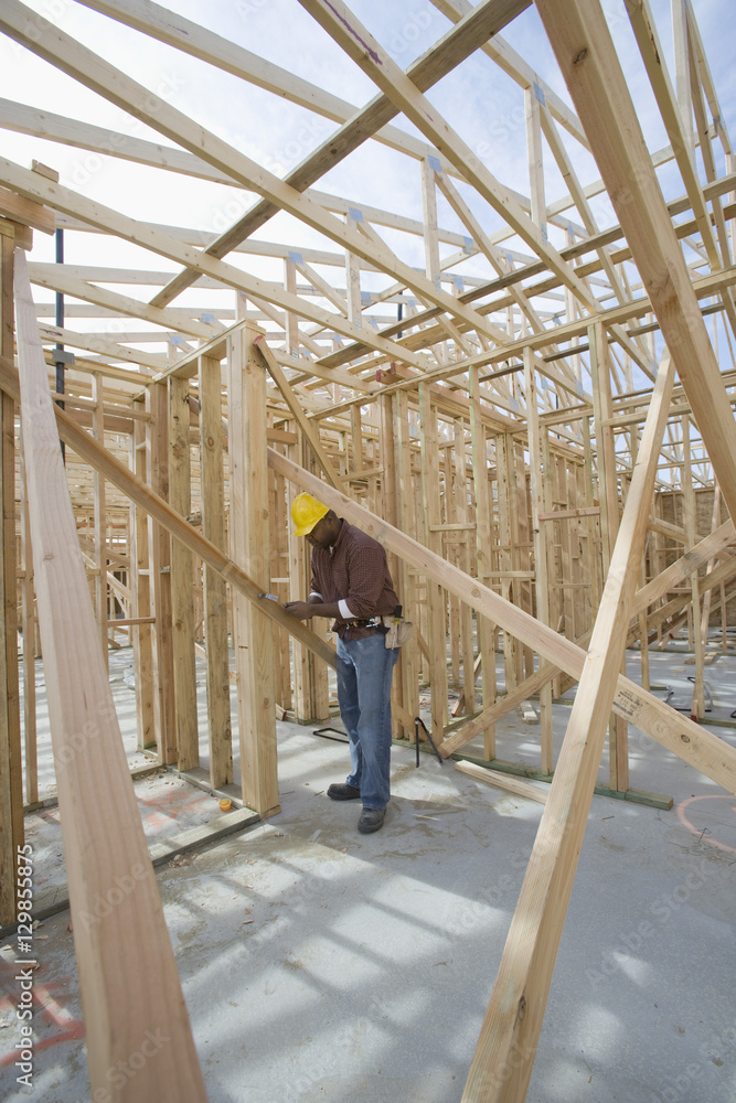 Full length view of a man measuring wooden beam in framework at construction site