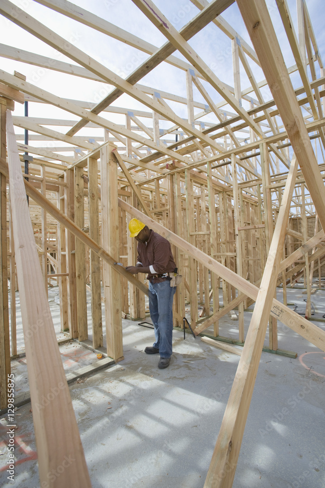 Full length view of a man measuring wooden beam in framework at construction site Full length view of a man measuring wooden beam in framework at construction site