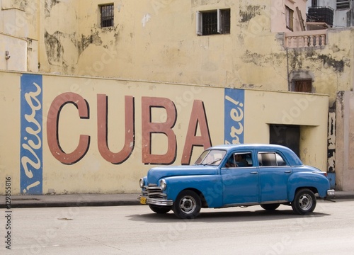 A vintage 1950's American car passing a 'Viva Cuba' sign painted on a wall in cental Havana, Cuba photo