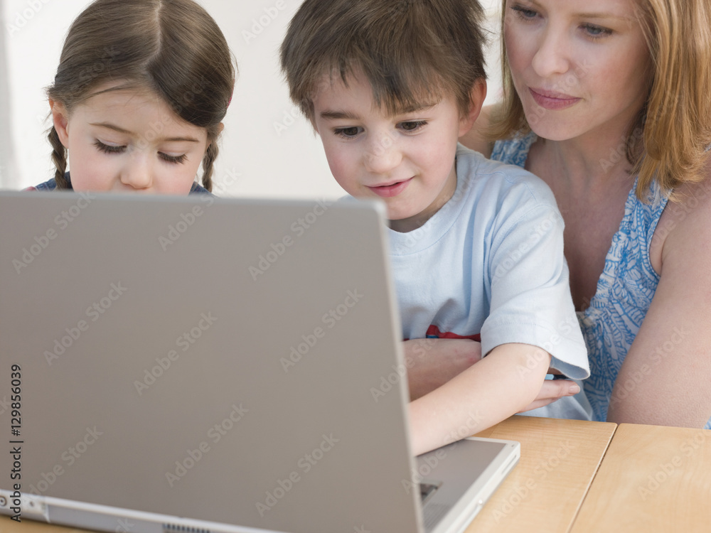 Mother and children using laptop at table in home Mother and children using laptop at table in home