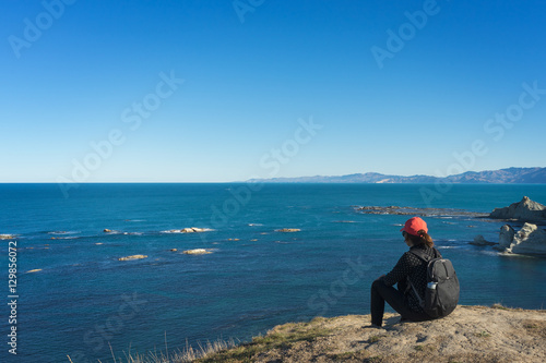 Young tourist woman sitting on the top of cliff and looking at a