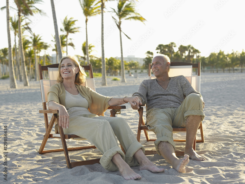 Fototapeta premium Full length of happy senior couple relaxing on deckchairs at tropical beach