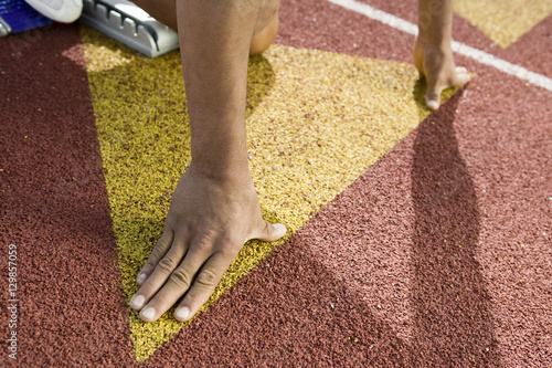 Cropped image of male athlete in starting block at racetrack