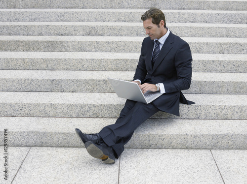 Full length of businessman using laptop of office steps