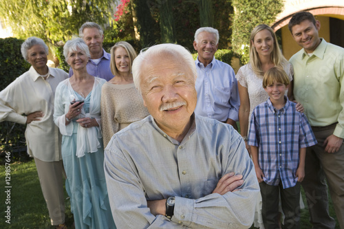 Portrait of happy senior man standing with hands folded and family in the background