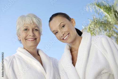 Portrait of two multiethnic women in bathrobes against blue sky at spa