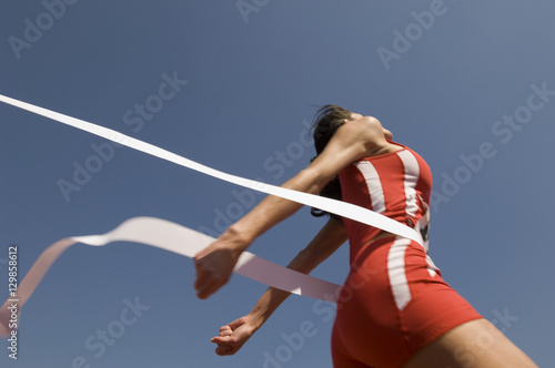 Valokuvatapetti Low angle view of young female athlete crossing finish line against clear blue s