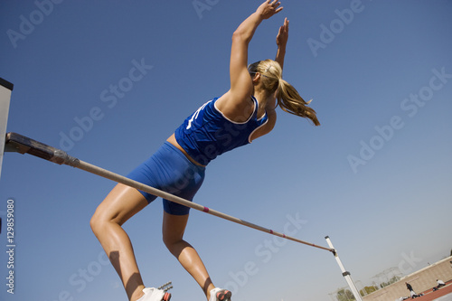 Low angle view of a female high jumper in midair over bar against blue sky