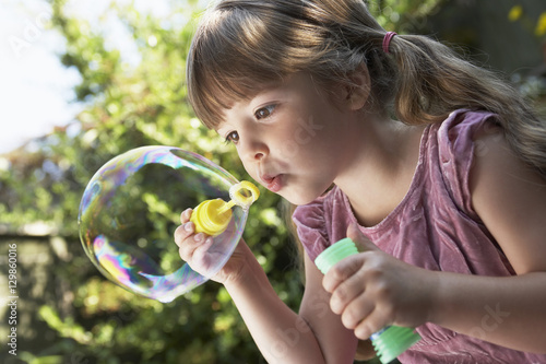 Closeup of a little girl blowing soap bubbles in the backyard
