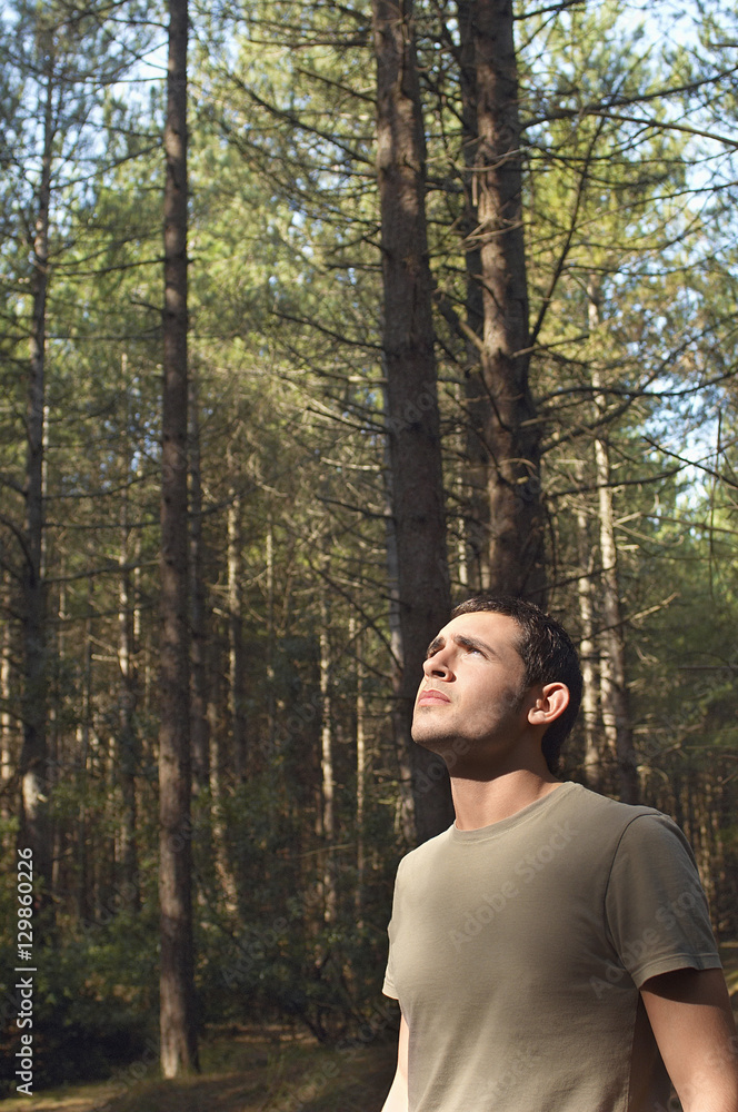 Worried young man looking up at trees in woods 