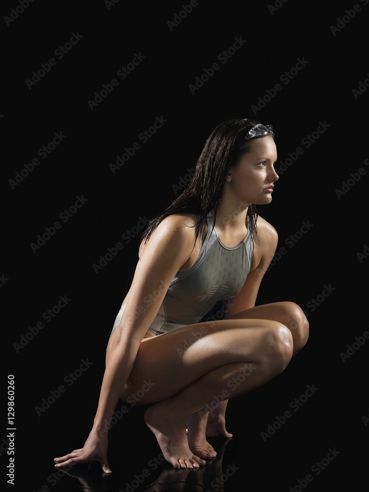 Full length side view of a female swimmer crouching against black background Full length side view of a female swimmer crouching against black background