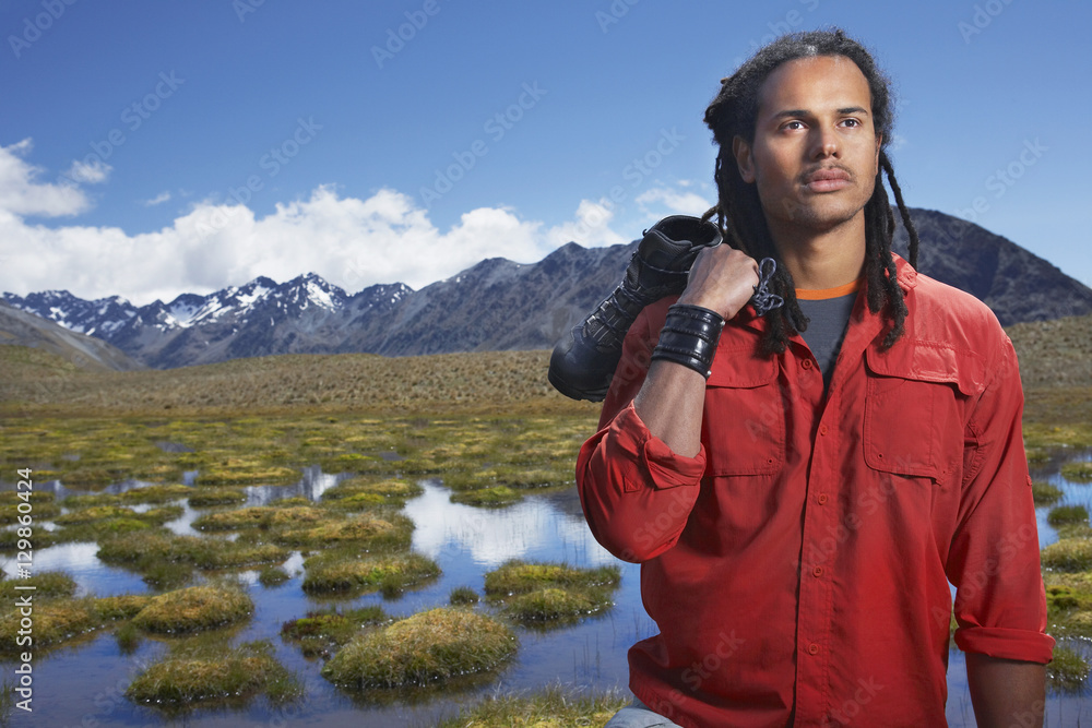 Mixed race man holding shoes by ponds against mountains