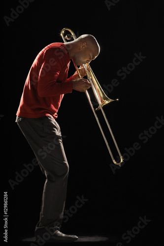 Side view of an African American man playing the trombone against black background