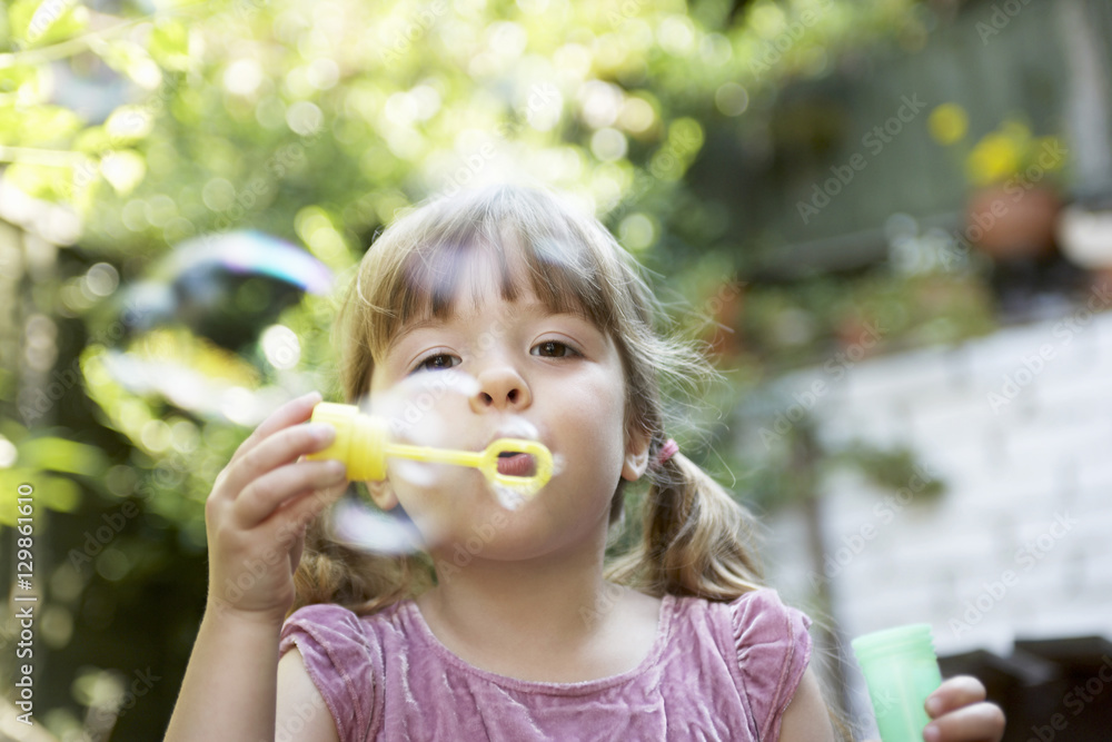 Closeup of a little girl blowing soap bubbles in the backyard
