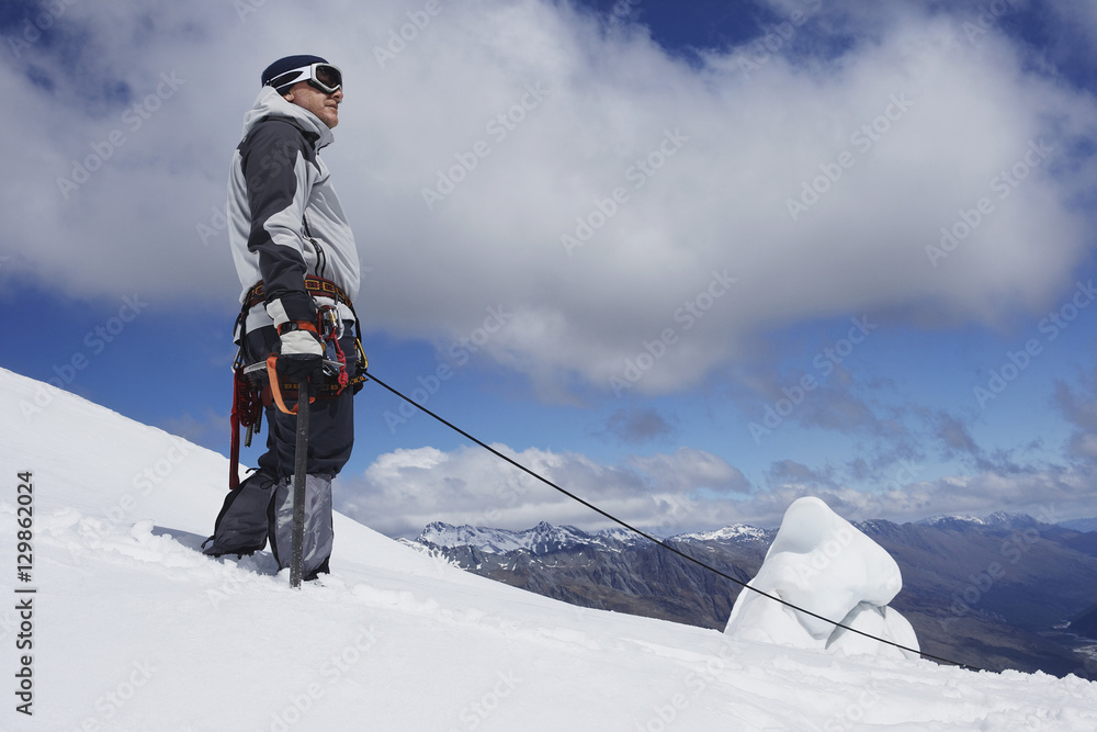 Low angle view of a male mountain climber standing on snowy slope with safety line attached