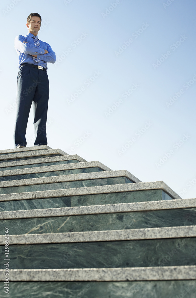 Low angle portrait of confident businessman standing on marble staircase against clear sky Low angle portrait of confident businessman standing on marble staircase against clear sky