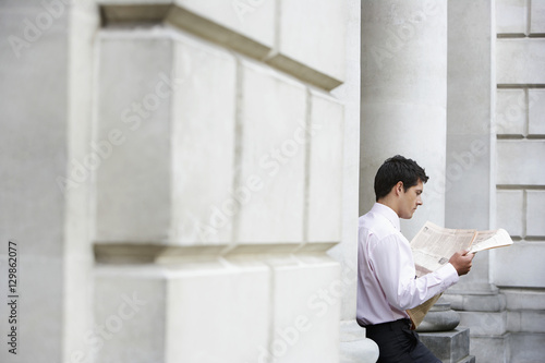 Photography Young businessman sitting on pillar reading financial newspaper