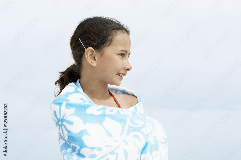 Happy little preadolescent girl wrapped in towel looking away while standing at beach Happy little preadolescent girl wrapped in towel looking away while standing at beach