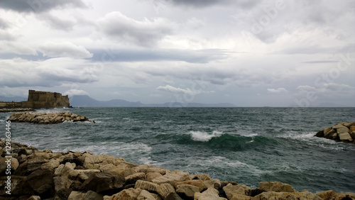 View of the restless Gulf of Naples with a great-looking wave and a castle (Castel Dell'ovo) in windy cloudy weather photo