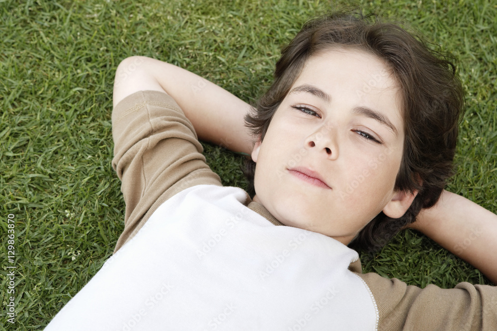 Closeup portrait of cute elementary boy with hands behind head lying on grass Closeup portrait of cute elementary boy with hands behind head lying on grass