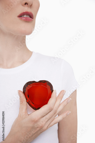 Fototapeta Naklejka Na Ścianę i Meble -  Closeup midsection of a woman in white tshirt holding red glass heart against white background