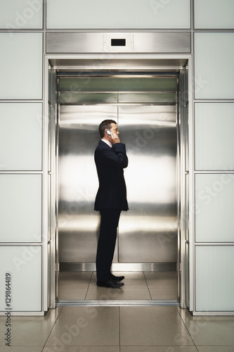 Profile shot of middle aged businessman using cellphone in elevator