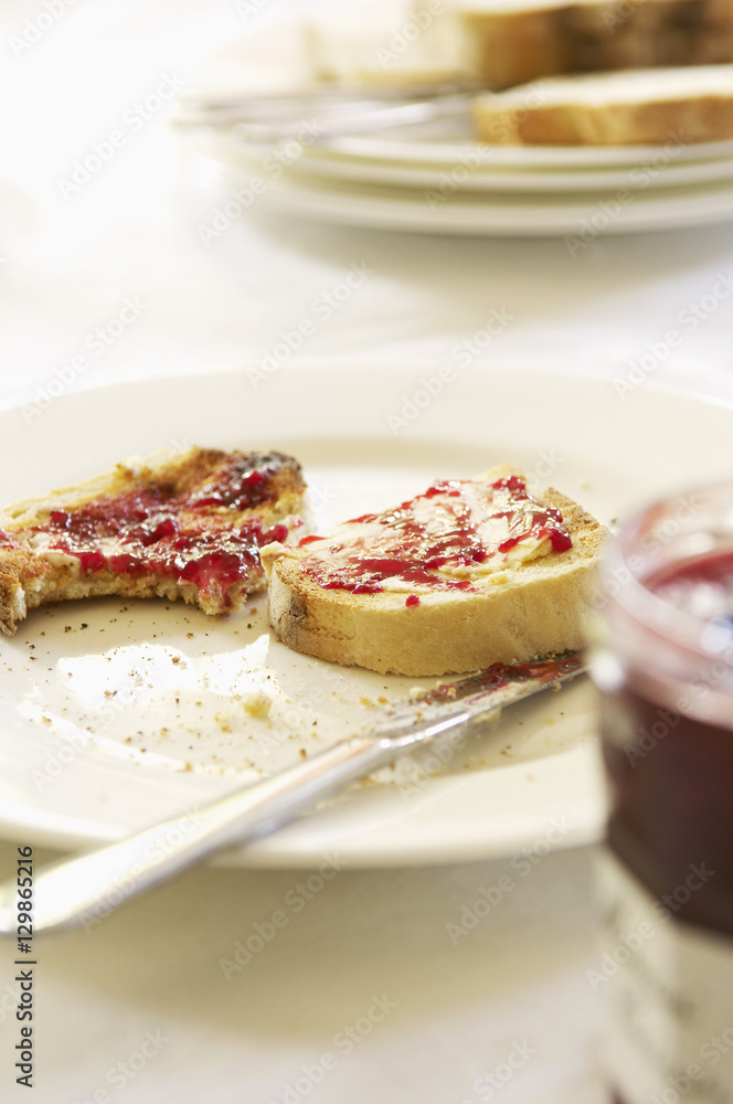 Closeup of a plate with half eaten toast covered in jam on table set for breakfast Closeup of a plate with half eaten toast covered in jam on table set for breakfast