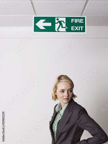 Young blonde businesswoman standing under exit sign in office