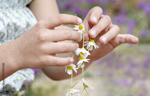 Closeup of girl's hands making flower necklace at field