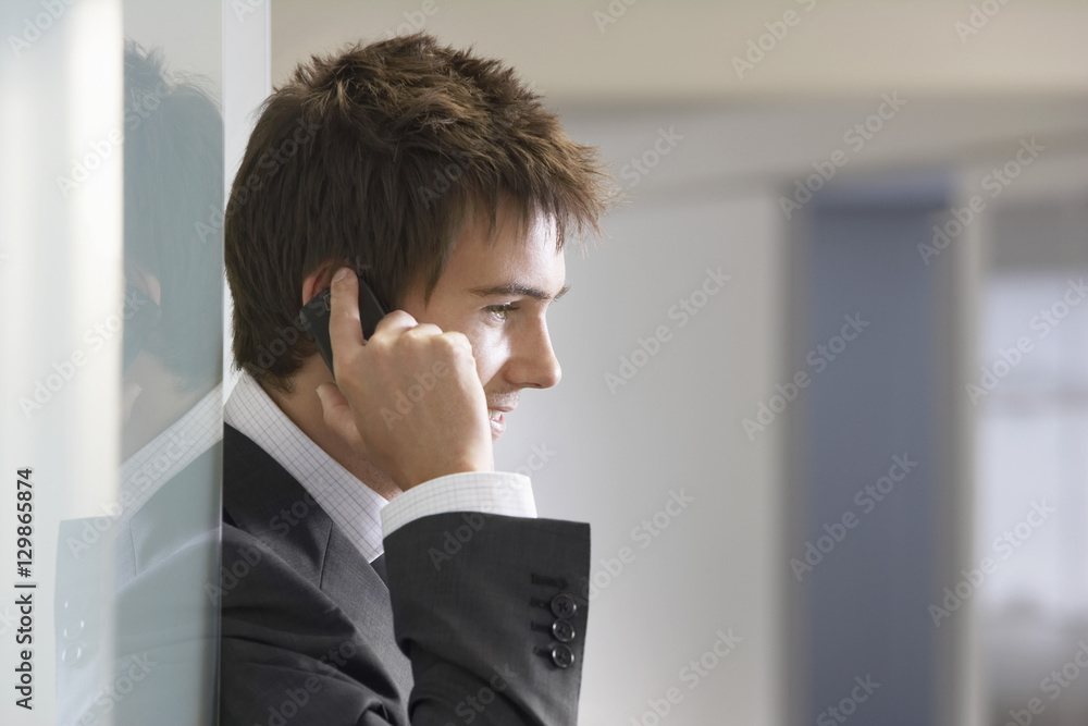 Closeup side view of a young businessman talking on cellphone in doorway Closeup side view of a young businessman talking on cellphone in doorway