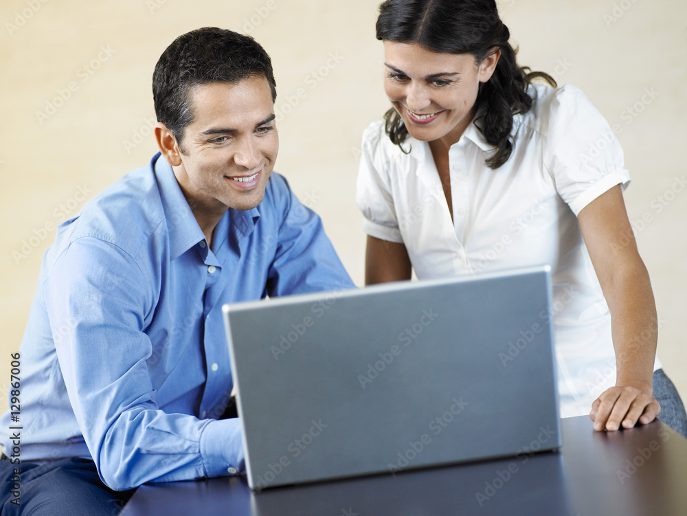 Happy businessman and businesswoman using laptop at desk in office Happy businessman and businesswoman using laptop at desk in office