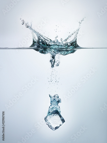 Ice cube splashing into clear water surface view