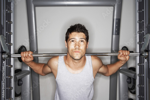 Portrait of young man struggling to lift weights at gym