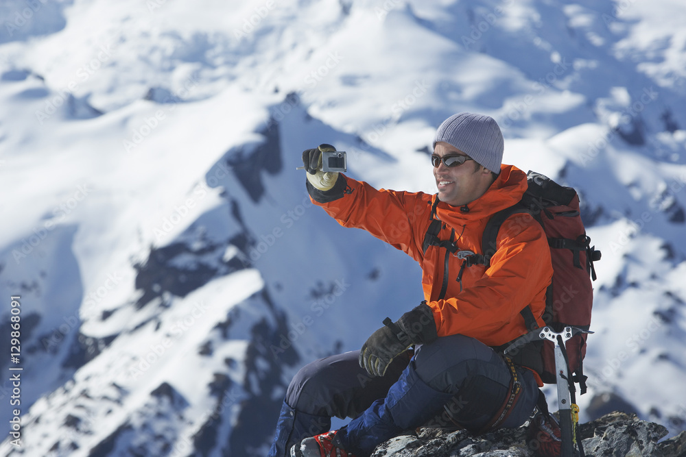 Side view of a male climber taking picture of snowy mountains