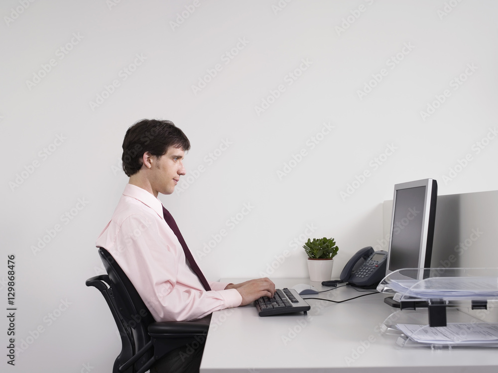 Side view of a male office worker using computer at desk in the office Side view of a male office worker using computer at desk in the office