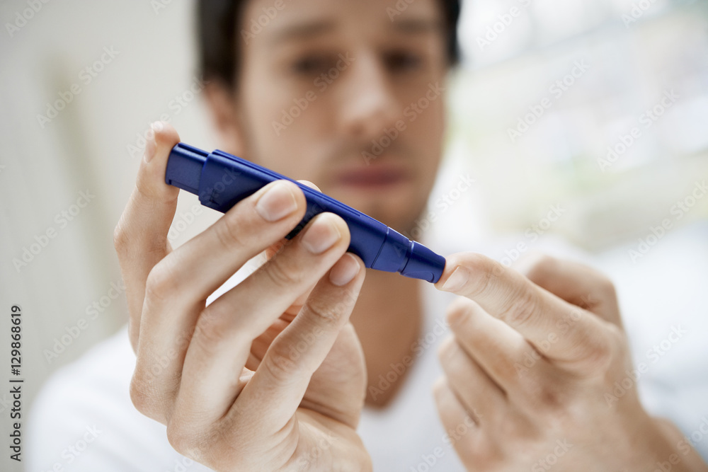 Closeup of young man using lancelet on finger in bathroom Closeup of young man using lancelet on finger in bathroom