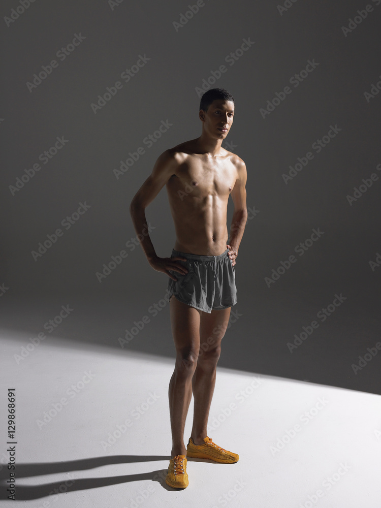 Full length of a shirtless confident young athlete standing against gray background Full length of a shirtless confident young athlete standing against gray background
