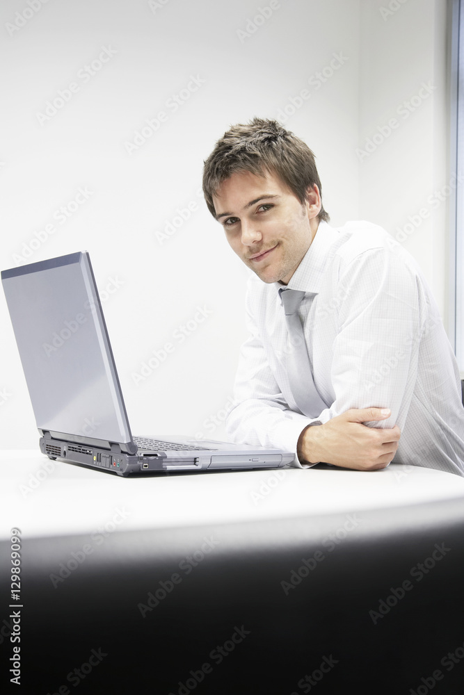  Portrait of a smiling young businessman sitting at desk with laptop