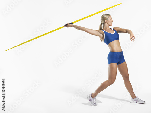 Full length side view of a female athlete preparing to throw javelin against white background photo