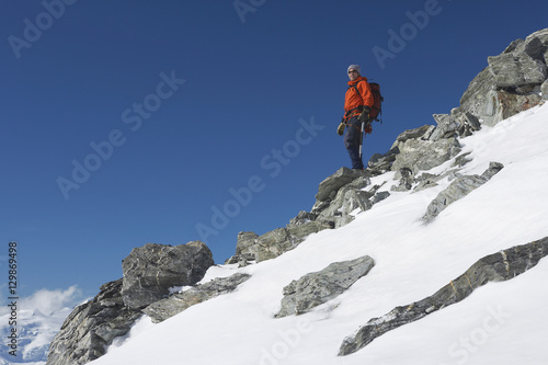 Low angle view of a male mountain climber descending snow and boulder slope