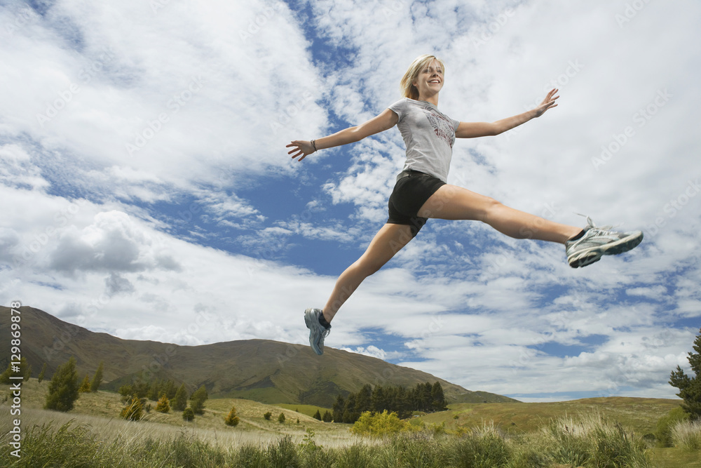 Low angle view of a young woman leaping on rural landscape