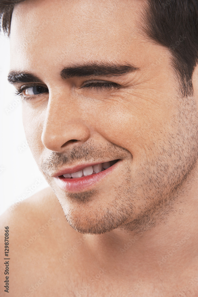 Fototapeta premium Closeup of flirtatious young man winking on white background