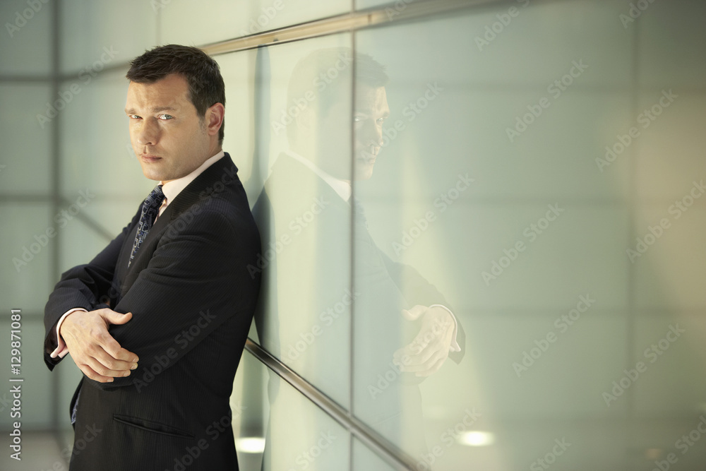 Portrait of confident middle aged businessman with arms crossed leaning on glass wall in office Portrait of confident middle aged businessman with arms crossed leaning on glass wall in office